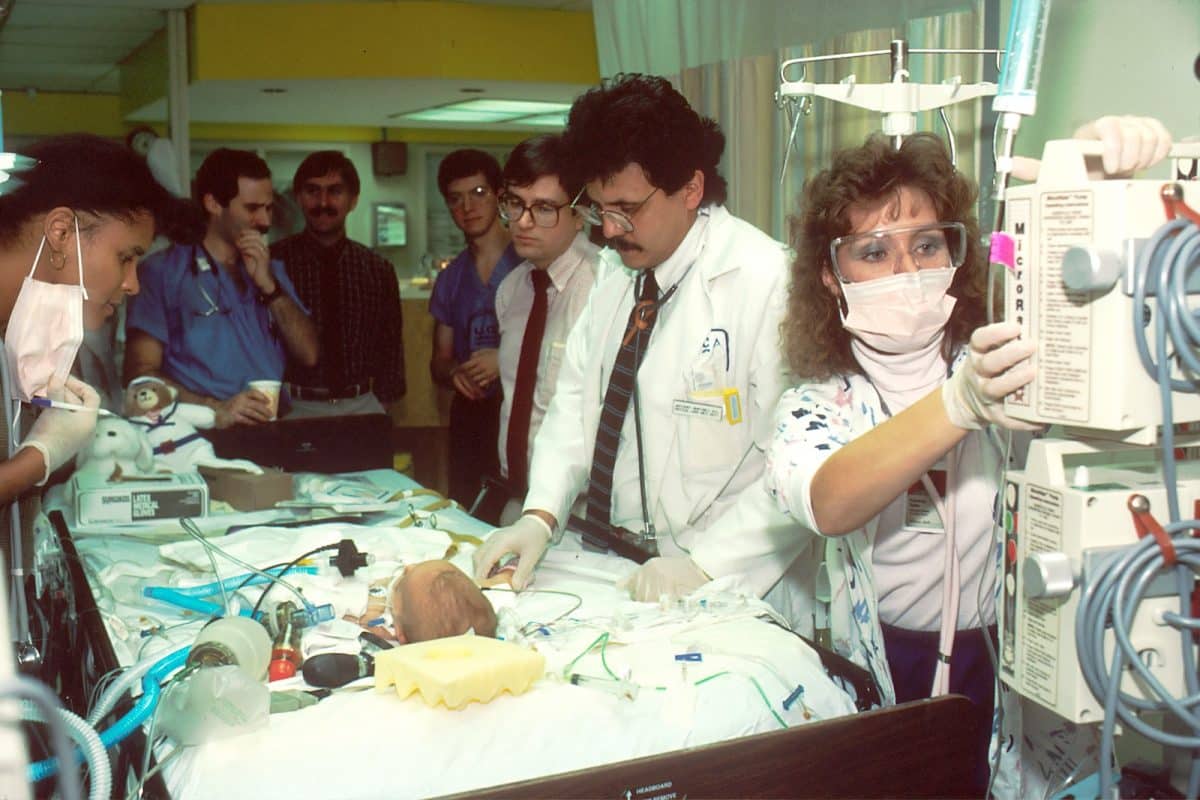 people beside baby lying on bed with medical apparatuses