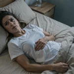 Femme allongée dans son lit la nuit, main posée sur le ventre avec une expression préoccupée, illustrant les mouvements abdominaux nocturnes