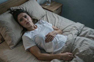 Femme allongée dans son lit la nuit, main posée sur le ventre avec une expression préoccupée, illustrant les mouvements abdominaux nocturnes